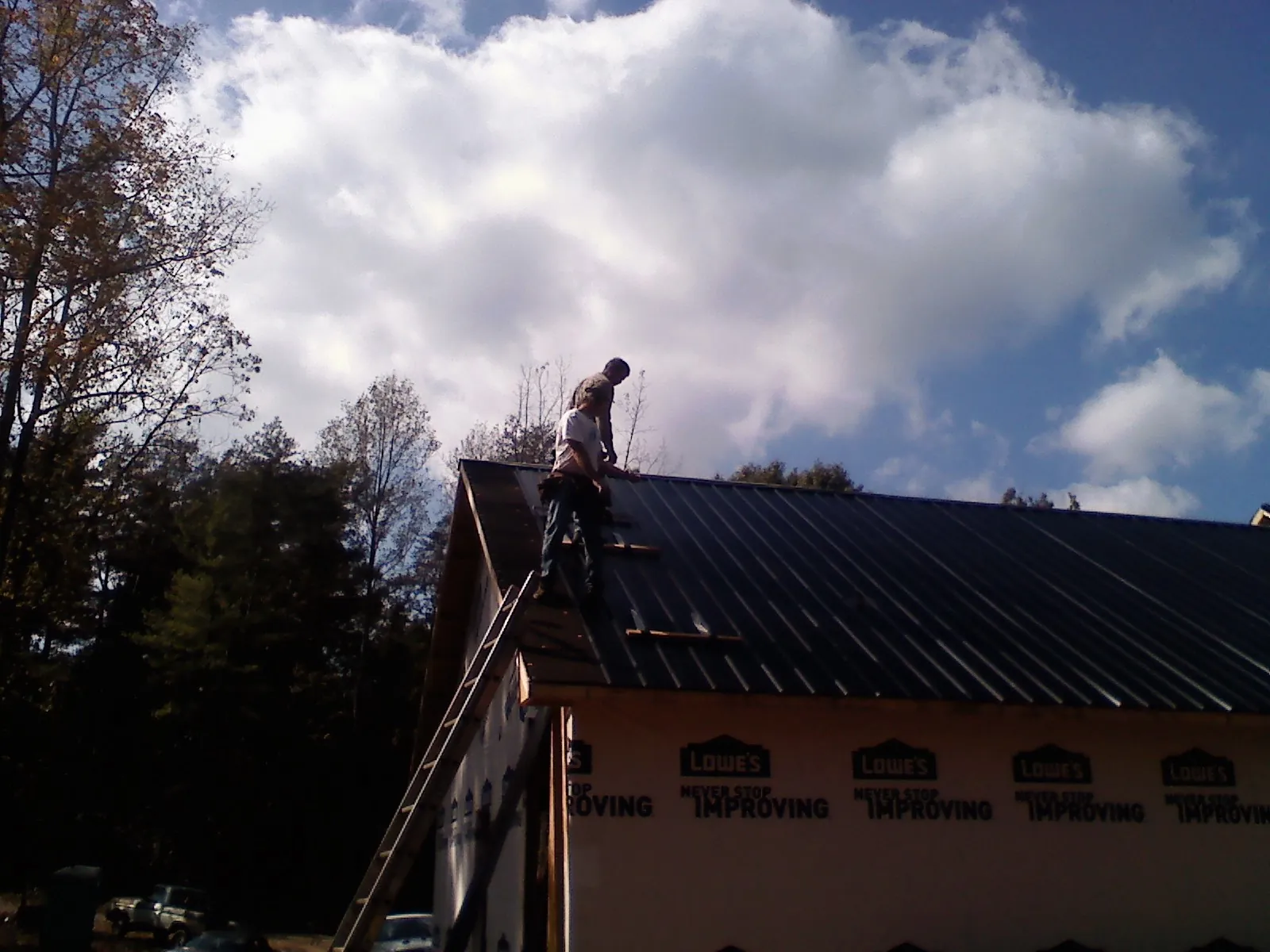 Roofer fastening dark metal panels high against a cloudy sky, from a Roof Inspection job in Tallassee
